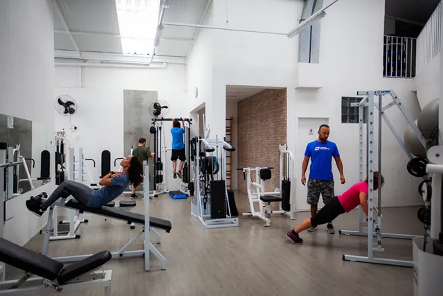 Sala de musculação da academia com alunos treinando e professor acompanhando